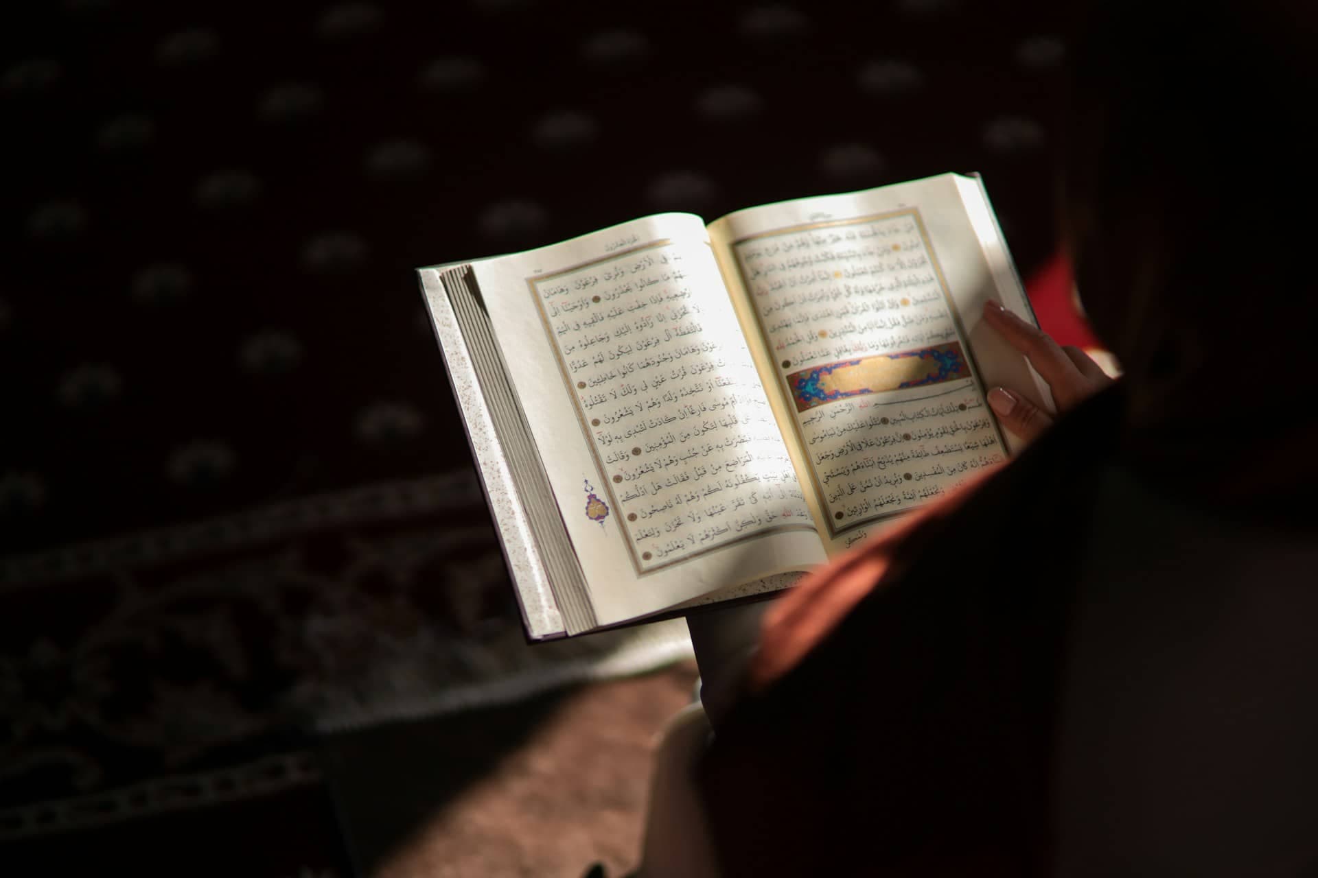A student reading from an open Quran in soft window light
